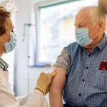 General practitioner giving flu shot to a senior man in clinic